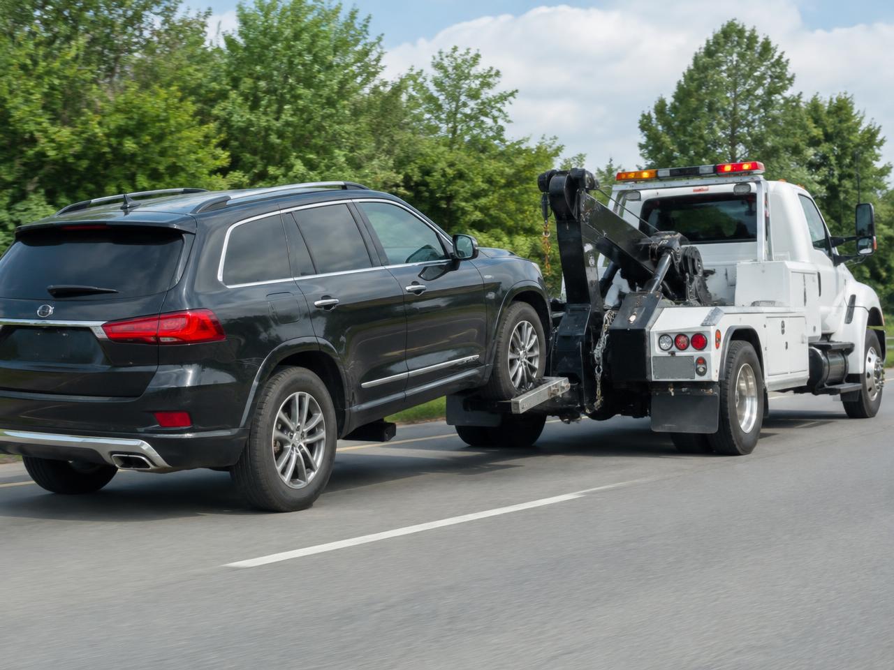 A black SUV being towed by a wheel-lift tow truck